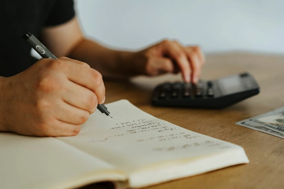A person smiling while writing financial goals in a notebook at a sunlit desk.